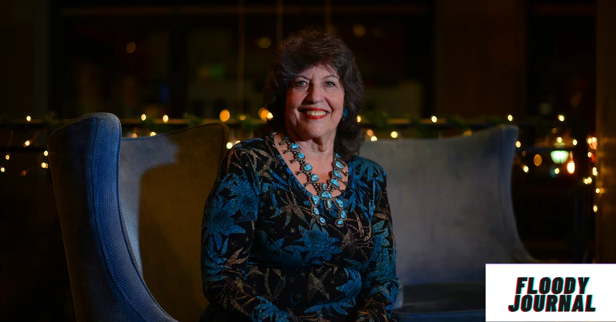 Carol Schwartz sitting on a blue chair in a patterned blue and black dress with a turquoise necklace, with warm string lights in the background. Meta description: Carol Schwartz biography—discover her age, height, net worth, family, and career highlights in 2025.
