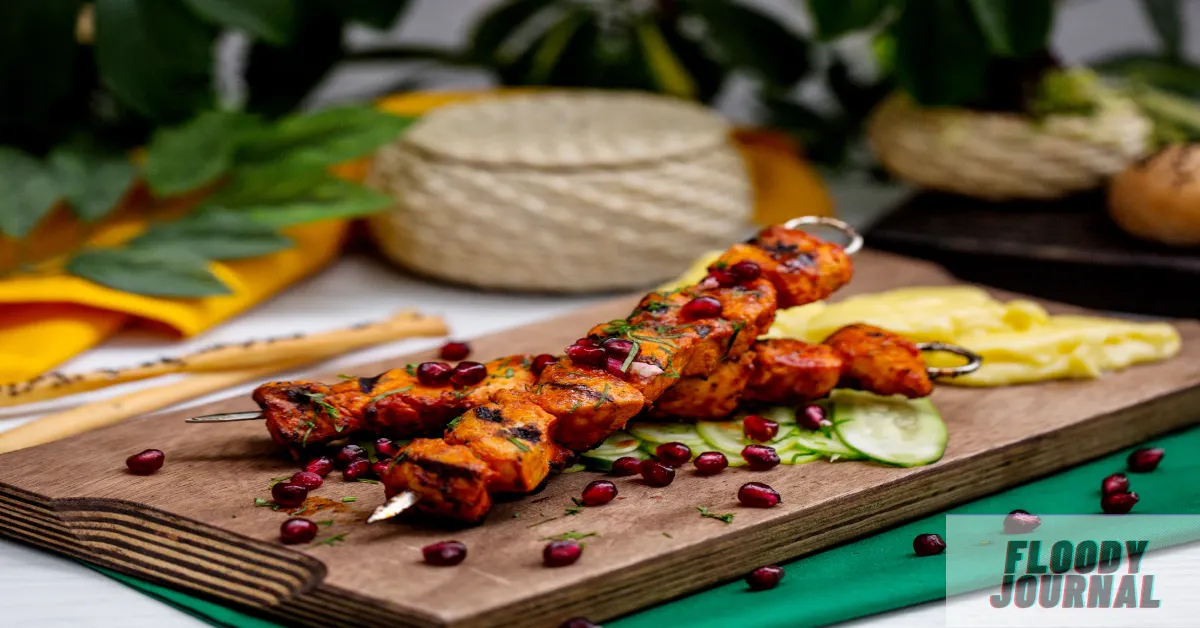 Grilled chicken tikka meat skewers on wooden board with pomegranate seeds, fresh herbs, and traditional naan bread in background